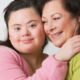 Photo of young adult woman with down syndrome hugging an elder female caregiver